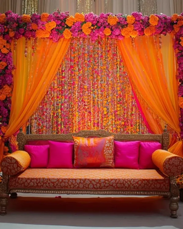 For a rich and royal mehendi, this setup combines a dense frame of bougainvillea-style flowers with shimmering gota patti curtains and a classic diwan.