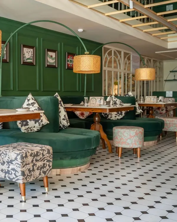 A full view of the custom furniture I created for "The Drawing Room" at Smoke House Deli. The setup includes curved green velvet banquettes, dining tables, and uniquely upholstered ottomans, all designed to fit the whimsical theme of the space.