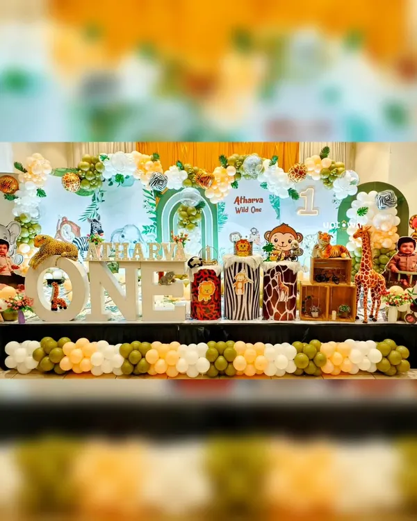 A full view of our 'Wild One' jungle safari theme, perfect for a first birthday. The stage includes a large backdrop, animal-print plinths, character cutout's of a lion, monkey, and giraffe, and a balloon garland in natural green's and white's.