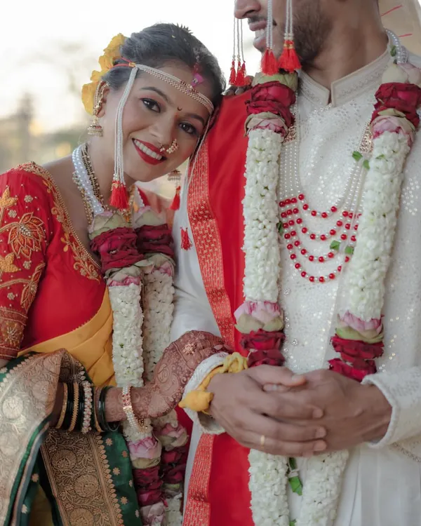 A radiant Maharashtrian bride rests her head on her groom's shoulder. This close-up highlights her beautiful smile, traditional nath, and the intricate details of their wedding garlands.