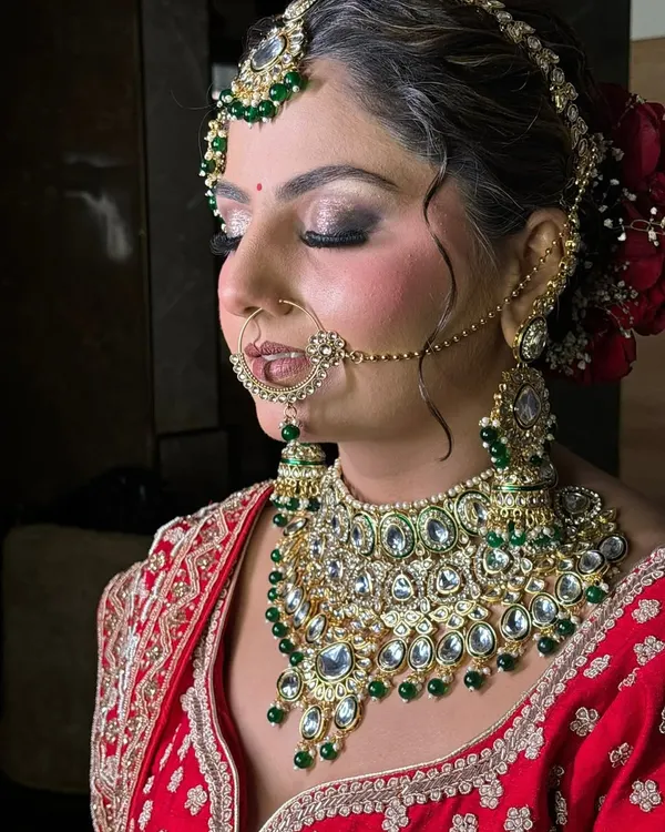 A side profile of a traditional bridal look, highlighting the contour, blush placement, and how the hairstyle with a red rose bun complements the entire ensemble.