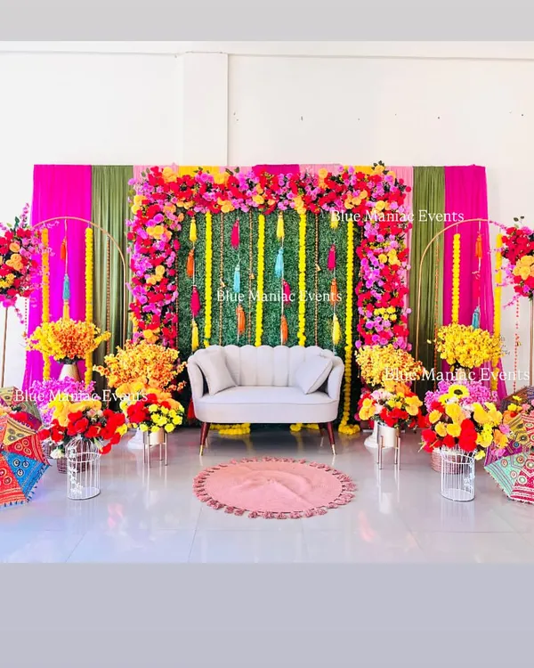 Our vibrant and colorful Mehendi setup is designed to create a festive and joyful atmosphere. This grand arrangement features a lush floral frame, a green backdrop with bright tassels, and is surrounded by an abundance of colorful flowers, perfect for large celebrations.