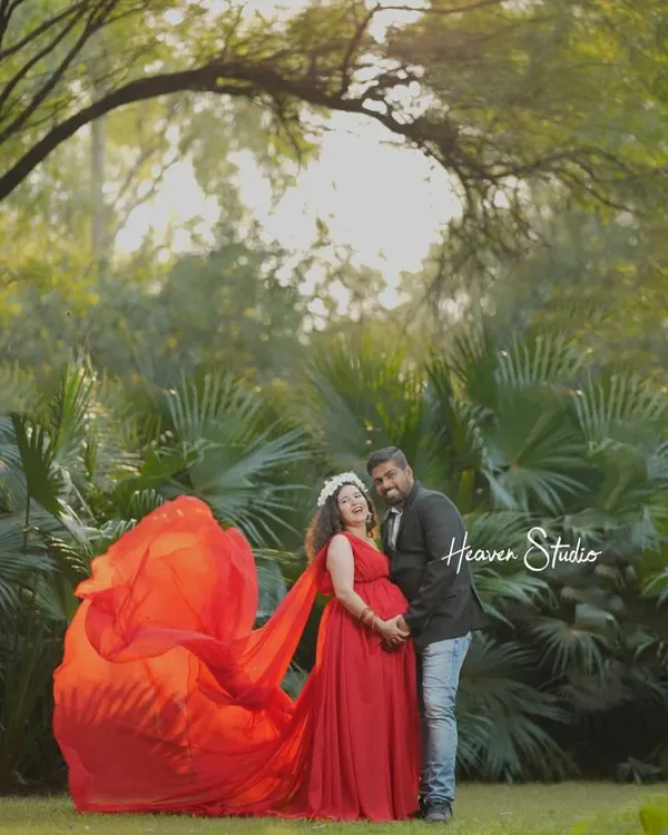 A beautiful portrait of a couple celebrating their love amidst nature. The vibrant red of her gown creates a stunning contrast with the lush greenery, making for a truly memorable outdoor maternity photo.