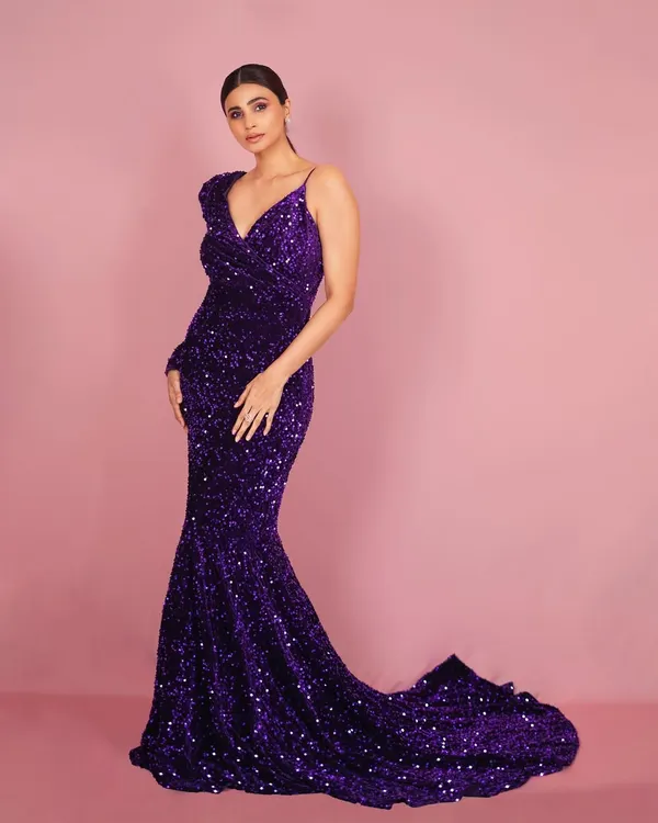 A full-length studio portrait of Daisy Shah. The simple pink background makes the vibrant purple of the sequin gown pop, creating a bold and memorable image for promotions.
