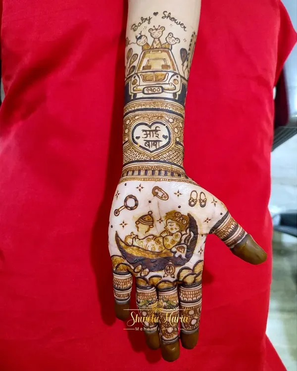 A close-up of a custom baby shower mehendi. This design features two babies sleeping on a crescent moon, surrounded by tiny footprints and rattles, with a special 'Aai Baba' heart motif on the wrist.