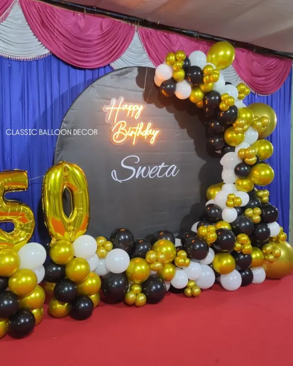 A classic 50th birthday setup with a black and gold theme, featuring a personalized circular backdrop, neon sign, and large foil number balloons.