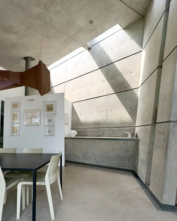 This is the dining area in our 'House of Stories' project, where shafts of natural light cut through the double-height space, transforming the raw concrete walls throughout the day. We designed this home as a sanctuary for a writer, where the interplay of light and shadow creates a quiet, contemplative atmosphere.