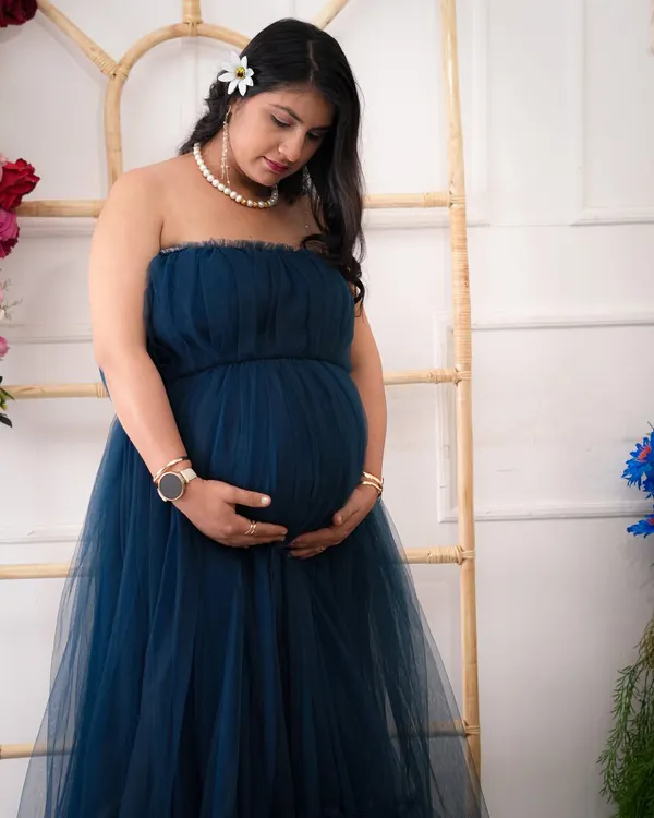 A quiet moment of reflection. This portrait captures the serene beauty of pregnancy, using soft lighting and a classic pose to highlight the mother's gentle connection with her baby.