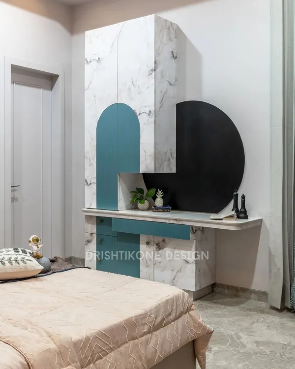 This kid's room combines playful design with practical features. The wardrobe unit includes a built-in desk and a unique circular blackboard for doodling, all finished in a chic white marble and pastel blue.
