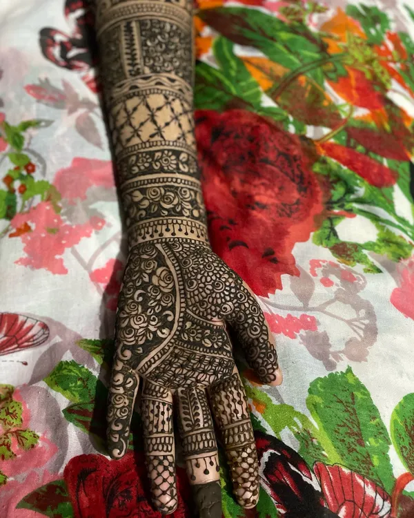 A complete bridal henna design from the fingertips to the forearm. This style features multiple bands with different patterns, including jaal netting, florals, and traditional leaf motifs.