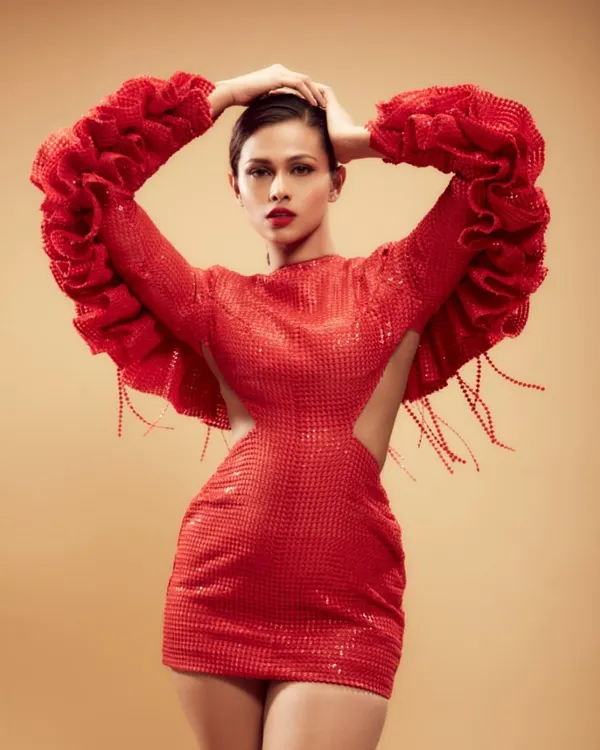 A full-length shot showcasing a dramatic red-on-red look for a high-fashion editorial. The makeup features a classic bold red lip and clean, defined eyes to complement the avant-garde styling of the structured gown.