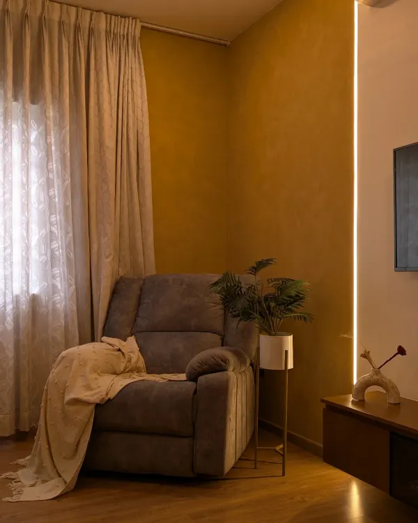 A cozy reading corner in a master bedroom, featuring a comfortable recliner and warm ambient lighting from a vertical LED strip.