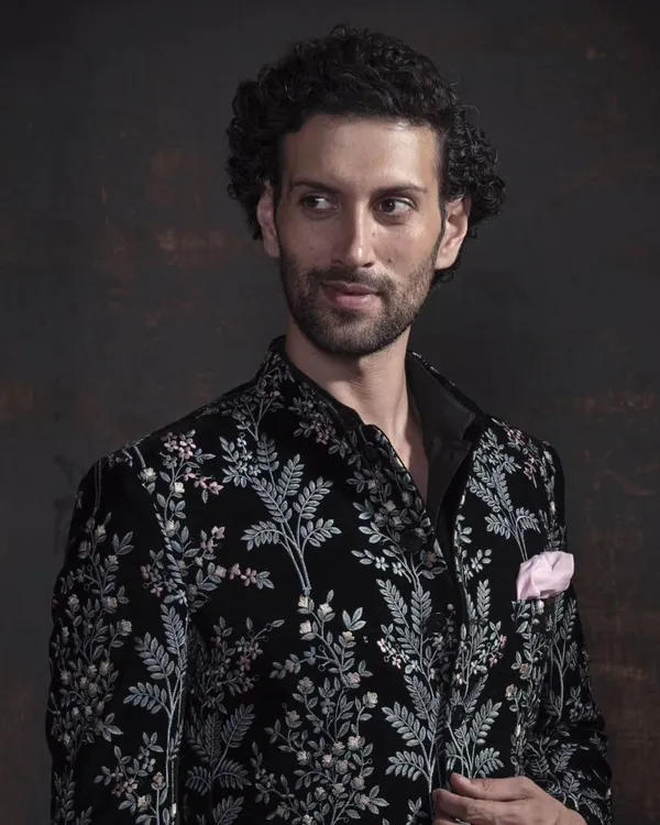 A close-up of the black velvet bandhgala with intricate silver floral embroidery. The craftsmanship is designed to be appreciated up close, showcasing the texture and detail.