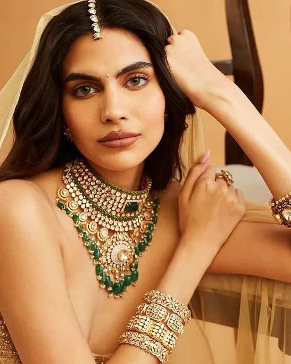 A stunning bridal look for Carbon Jewellery, featuring a warm, bronzed smokey eye and a neutral lip. The makeup enhances the model's features while complementing the heavy polki and emerald necklace.