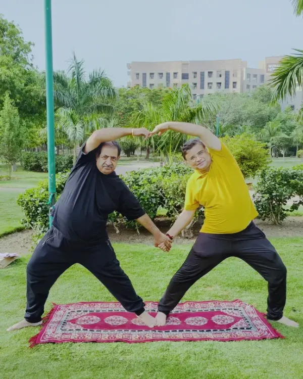Two students form a heart shape with their arms while holding a partner standing pose in a park. This image perfectly captures the connection and playfulness we cultivate in our outdoor yoga sessions.