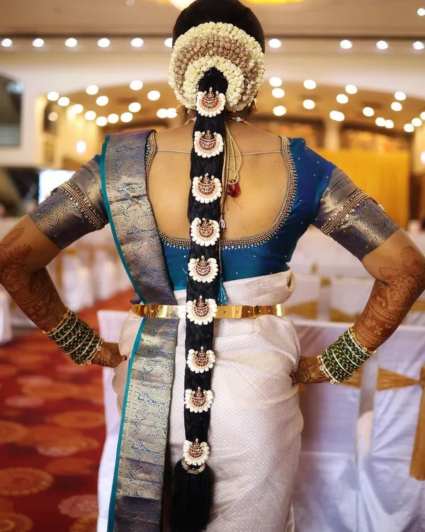 A classic South Indian bridal braid, or Poola Jada. This hairstyle features a neat braid adorned with jasmine flowers and traditional billai ornaments, creating a timeless and elegant look from the back.