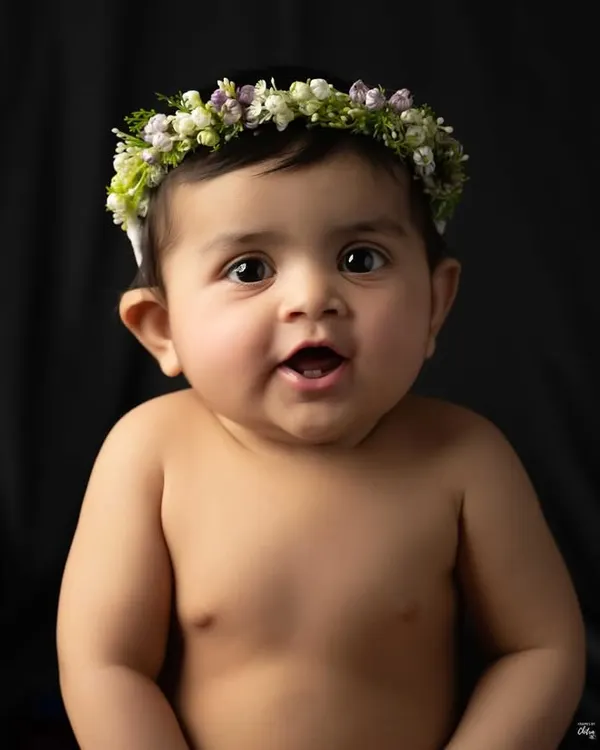 A simple, beautiful baby portrait against a classic black background. Wearing a delicate floral headband, her bright, curious eyes are the complete focus of the image.