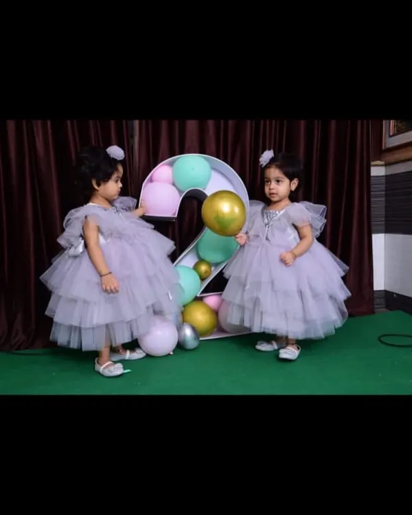 Twin sisters celebrating their second birthday in identical lavender layered gowns. These frocks are designed with soft tulle and flutter sleeves, making them perfect for little ones.