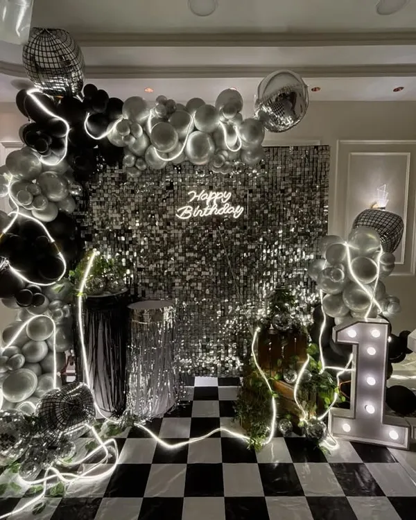 I create stunning, Insta-worthy backdrops that become the highlight of your party. This glam disco theme for a 13th birthday features a silver shimmer wall, a custom neon sign, a black and silver balloon arch with disco balls, and large marquee numbers.