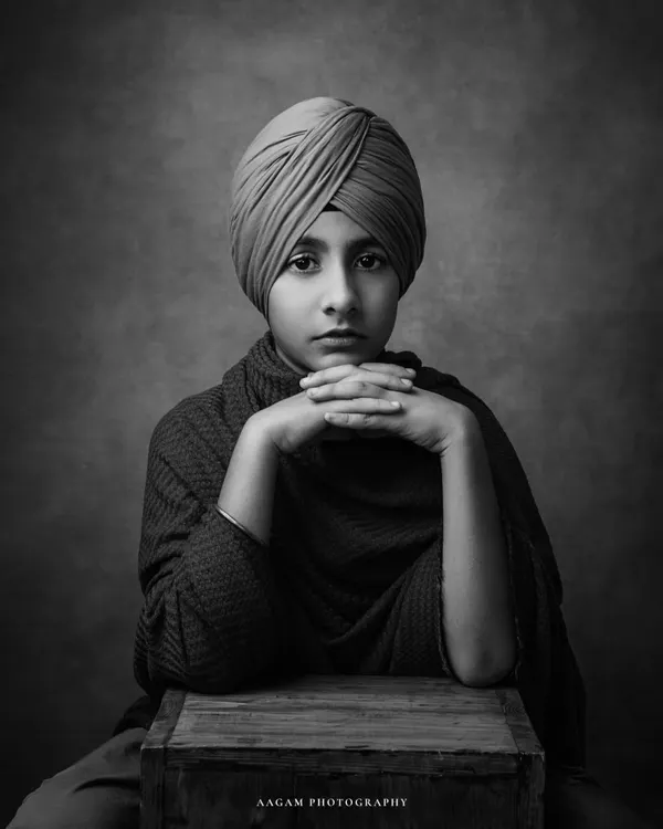 A powerful and poised portrait of a young boy. The black and white format emphasizes his strong gaze and the beautiful details of his turban, creating a timeless and striking image.