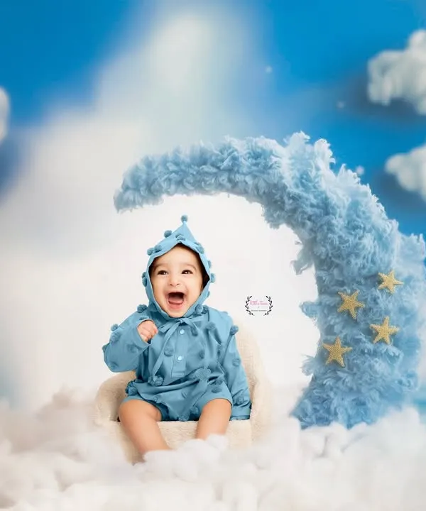 Over the moon with happiness! This adorable baby is all smiles, sitting on a fluffy blue crescent moon surrounded by clouds and stars. It's a truly dreamy and joyful setup.