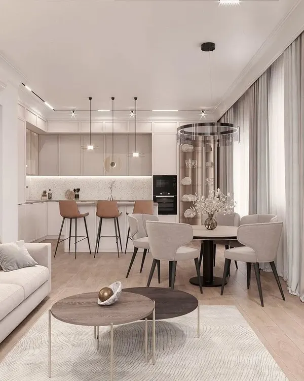This view showcases the seamless integration of an L-shaped kitchen with the main living area. By using a consistent neutral palette and warm wood flooring throughout, the entire space feels unified and expansive. The design includes a breakfast bar for casual seating and layered lighting to define each zone.