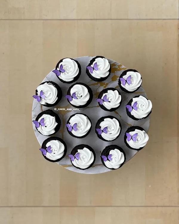 A top-down view of our popular butterfly cupcakes, with delicate purple butterflies on swirls of white frosting.