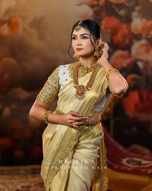 A model looking regal in a classic off-white and gold Kanjeevaram saree. The look is completed with a heavily embroidered blouse and traditional temple jewellery, perfect for a South Indian bride.