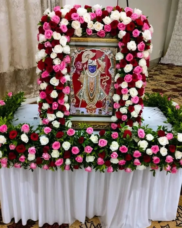 We create beautiful floral frames for deities to make your home pooja special. Here, a portrait of Shrinathji is adorned with a dense arch of fresh roses, creating a sacred and beautiful focal point for prayers.