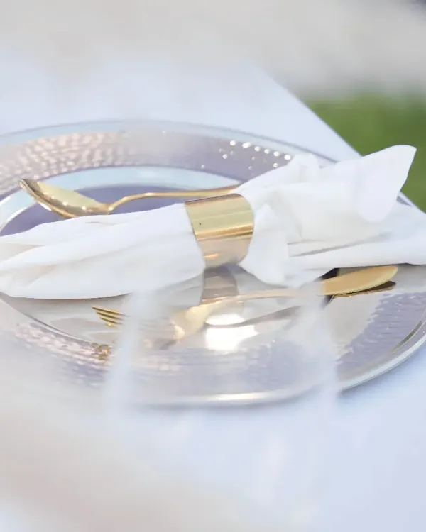 An elegant table setting featuring a hammered silver charger plate, gold-plated cutlery, and a crisp white napkin held by a gold ring. These small details contribute to a luxurious dining experience.