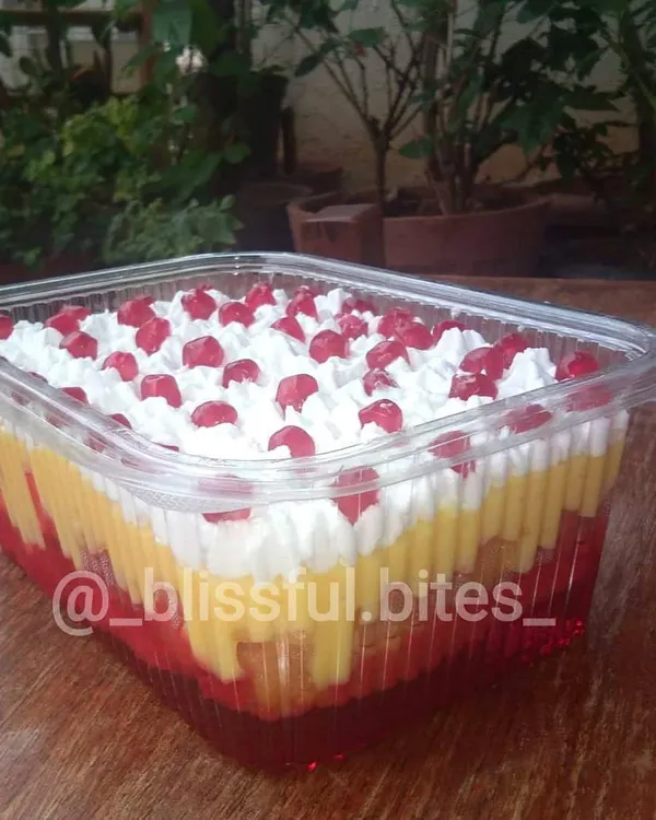 My Mixed Fruit Trifle in a party-sized container, showing the distinct layers of red jelly, yellow custard, and white cream, topped with pomegranate seeds.