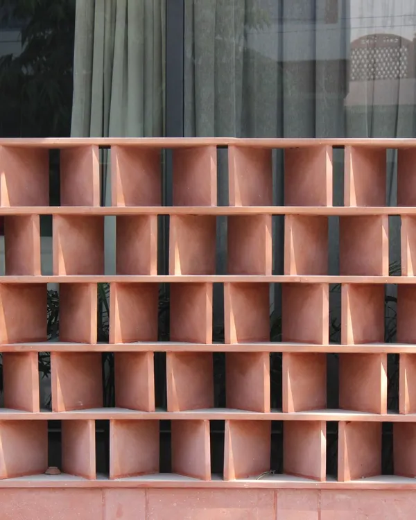 A close-up of the red sandstone jali from the Jaipur House. Each block is angled to filter the harsh sun while allowing for ventilation, a modern interpretation of a traditional Rajasthani architectural element.