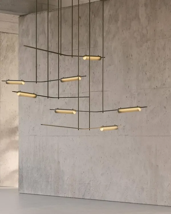 The Volant chandelier by Ross Gardam, a kinetic sculpture of brass bars and tubular glass, creates an elegant equilibrium in this concrete-walled space. Its form gives the impression of objects in motion, providing a captivating yet soothing focal point.