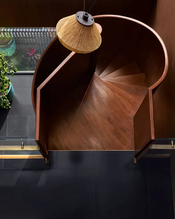 An overhead view of the spiral staircase at the Urban Hearth residence. Crafted in matte black metal and polished wood, its form is a gentle, turning ascent that anchors the double-height space while maintaining a sense of lightness and air.
