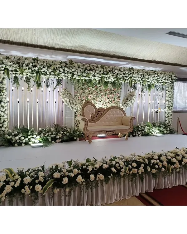 A classic and elegant all-white floral stage for a reception or engagement. The dense flower wall and classic sofa create a timeless look.