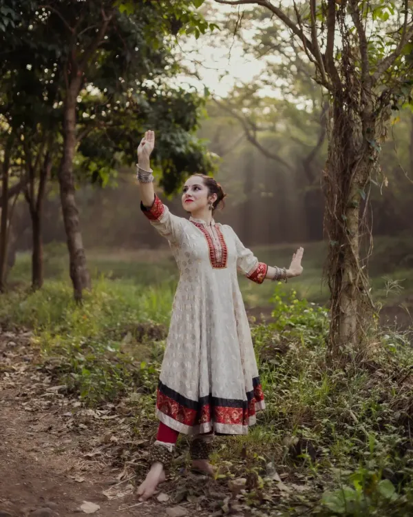 A full-length portrait of a Kathak dancer in a classic pose. The forest setting with rays of light filtering through the trees adds a magical quality to this performance portrait.