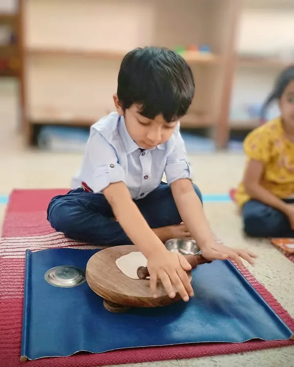 A child practices rolling dough, a practical life activity that strengthens hand and wrist muscles, preparing them for writing. This is also a wonderful sensory experience that builds coordination and focus.