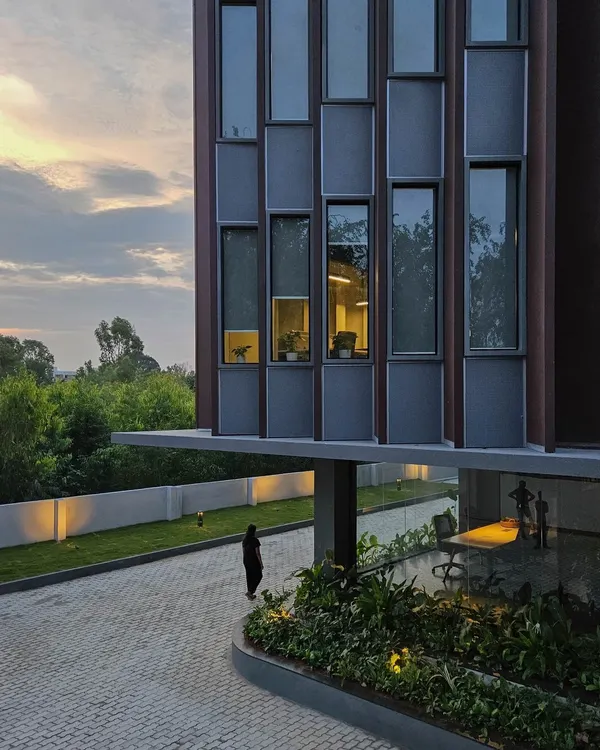 The building's facade at dusk, highlighting the interplay between the cantilevered entrance canopy and the gridded window pattern. This view shows how we integrate landscape and lighting to enhance the architectural form.