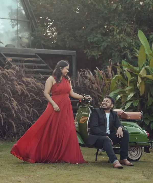 A couple poses with the vintage scooter in the garden. The vibrant red of the gown stands out against the green lawn and plants, showing how the space is perfect for colorful, lively photoshoots.