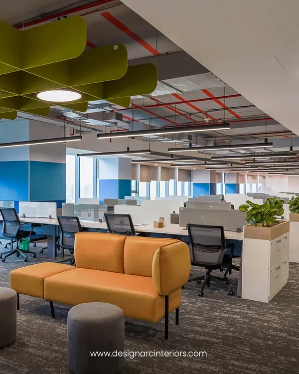 This open-plan office features bench-style workstations that promote teamwork, complemented by a comfortable lounge area for informal discussions. The design uses natural materials and plants to create a warm and productive atmosphere.