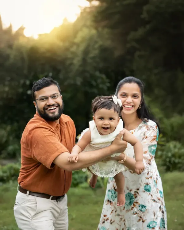 A happy family plays together in a park, with the parents lifting their daughter in the air. The golden hour sunlight creates a warm, magical glow.