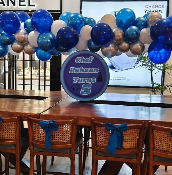 A simple yet cheerful balloon garland in shades of blue and silver, hung over a long table for a 5th birthday celebration.
