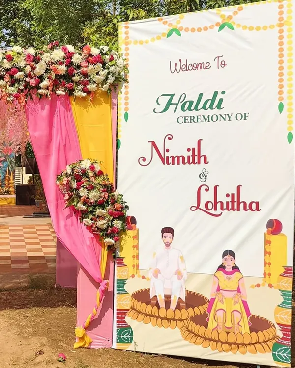 I design custom welcome boards like this one for a Haldi ceremony, featuring caricatures of the couple and event details. It's framed with matching floral arrangements.