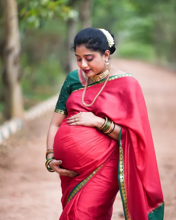 An absolutely stunning outdoor portrait of a mom-to-be in a traditional red and green silk saree. The way she holds her baby bump is so full of love and grace.