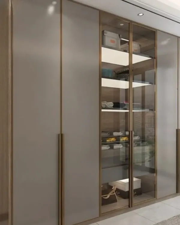 An elegant floor-to-ceiling wardrobe design. It features a mix of matte grey shutters and glass doors with a sleek metal frame, allowing for both concealed and visible storage.