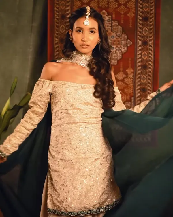 A full-length shot from a "Heeramandi" inspired photoshoot. I created a regal and vintage hairstyle with soft waves and a traditional maang tikka to complement the off-shoulder ethnic outfit.
