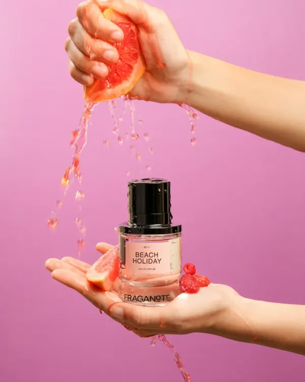 A dynamic action shot capturing a juicy splash of grapefruit over a bottle of 'Beach Holiday' perfume. We use high-speed photography to freeze motion, creating vibrant and energetic visuals that make products feel fresh and exciting.