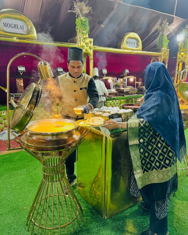 A guest is served a hot meal at my Mughlai food station. The setup features elegant golden chafing dishes and professional staff in traditional attire.