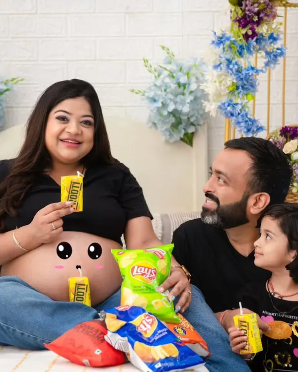 A fun and quirky family portrait celebrating pregnancy cravings. Sharing snacks and juice boxes, this family's playful energy is infectious. The cute drawing on the baby bump adds a whimsical touch.