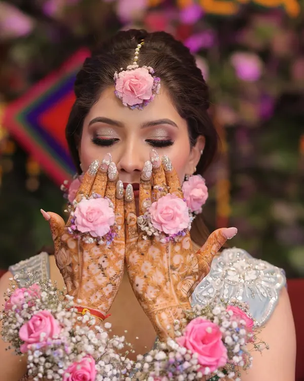 A beautiful shot capturing the essence of a Mehndi ceremony. The makeup features soft, shimmery eyes that complement the intricate henna and floral jewelry, creating a look that is both traditional and stunning.